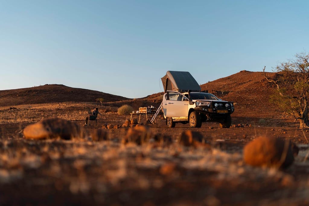 Geländewagen mit Dachzelt und Campingplatz in der roten Wüstenlandschaft von Palmwag, Namibia bei Sonnenuntergang.