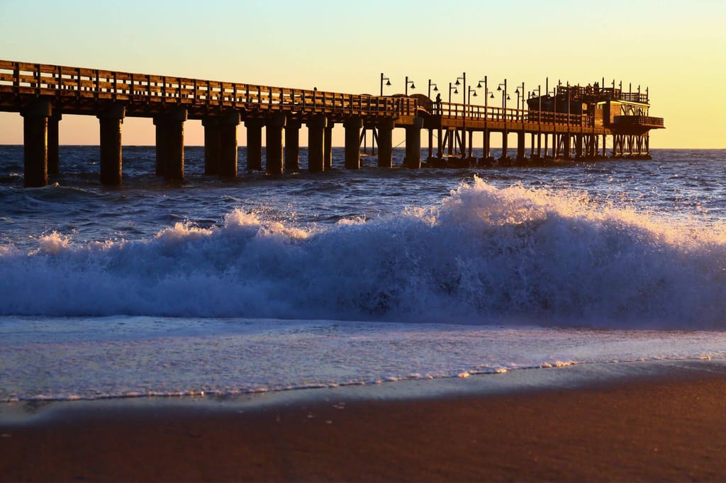 Holzsteg in Swakopmund bei Sonnenuntergang, Wellen brechen am Strand