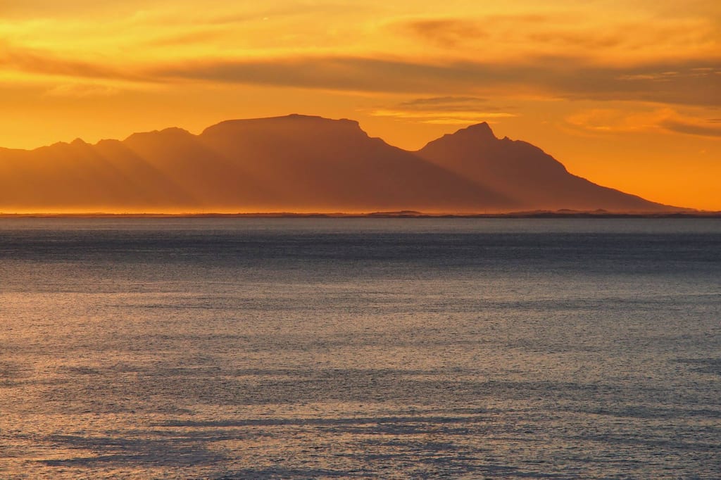 Meeresfläche vor einer fernen Gebirgskette in goldenem Sonnenuntergangslicht