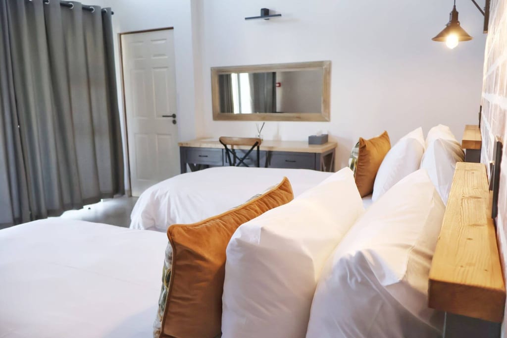 Helles Doppelzimmer mit weißen Betten, braunen Zierkissen und Schreibtisch im Hintergrund.