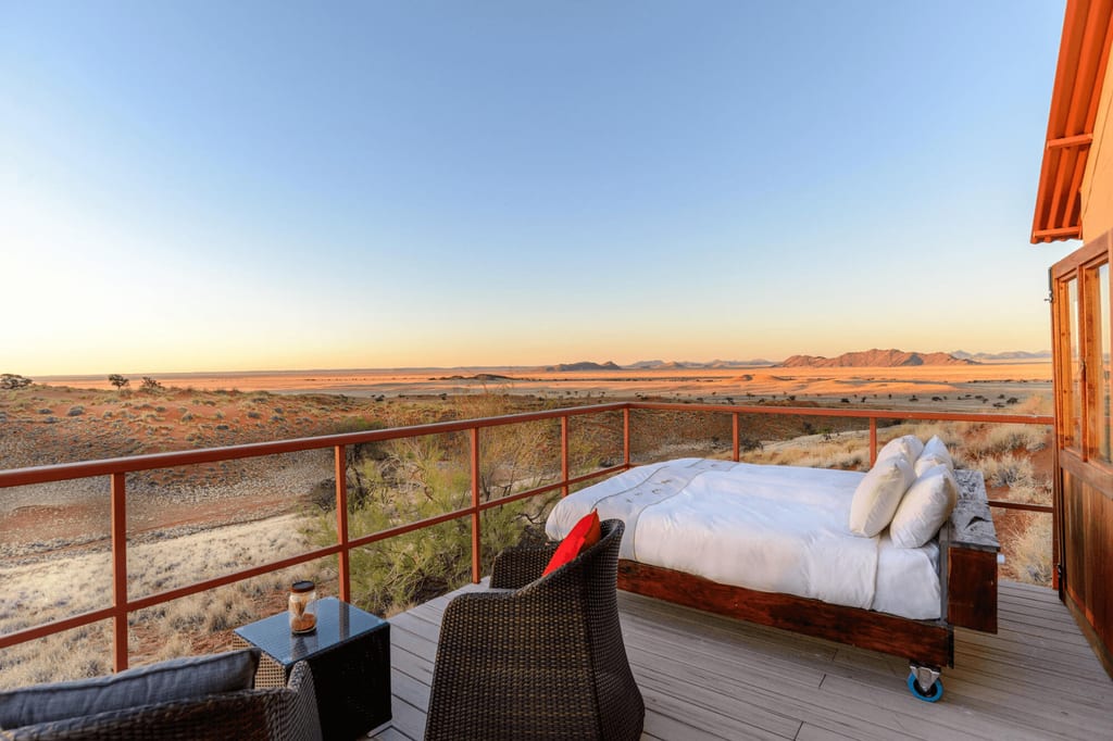 Terrasse mit Bett und Sitzmöbeln über weiter, golden beleuchteter Wüstenlandschaft bei klarem Himmel