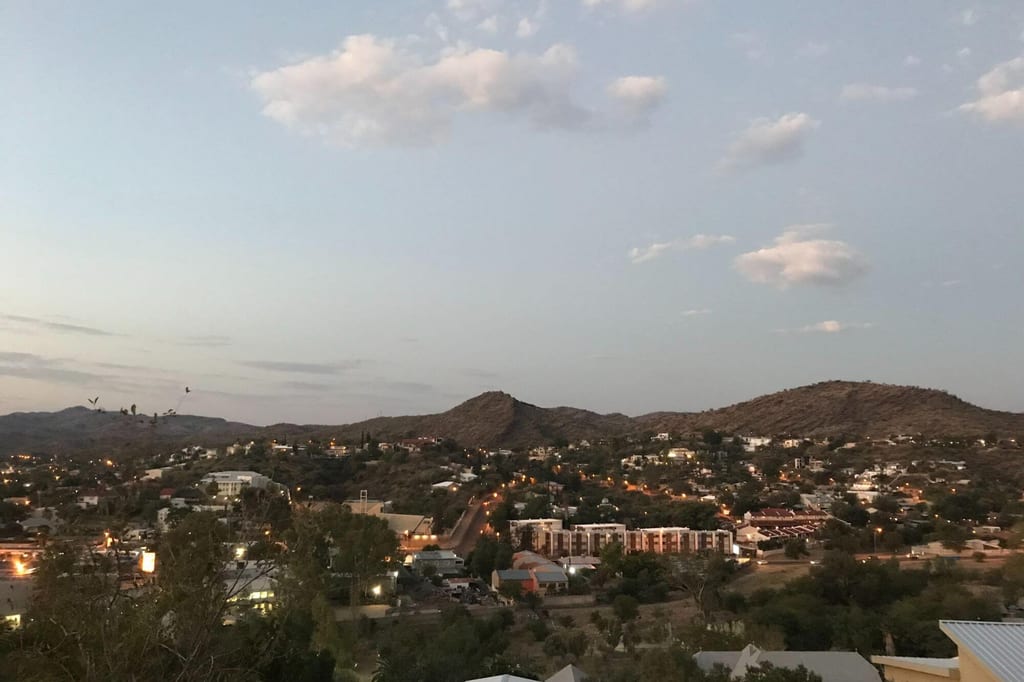 Abendlicher Panoramablick auf eine Kleinstadt im Binnenhochland Namibias mit Hügeln und Straßenlichtern