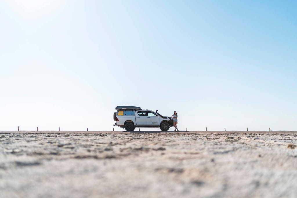 Weite Salzpfanne in Halali, Namibia, mit Geländewagen und einer Person bei klarem Tageslicht.