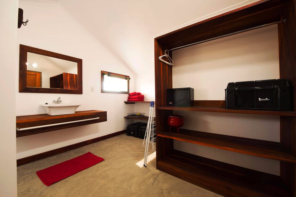 Helles Ankleidezimmer mit offenem Holzregal, Waschbecken, rotem Handtuch und Fensterlicht.