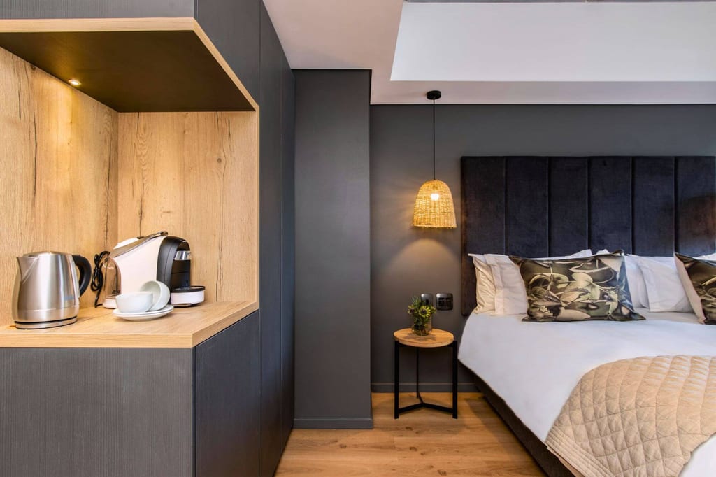 Modernes Hotelzimmer mit Doppelbett, Nachttisch und Kaffee-/Teestation in warmer Beleuchtung.