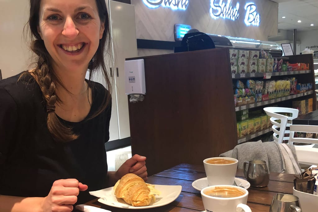 Lächelnde Frau sitzt im Café am Tisch mit Croissant und zwei Tassen Kaffee