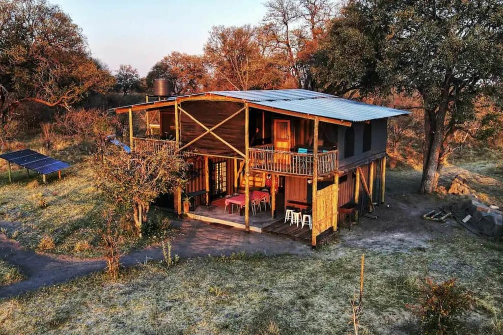 Zweistöckige Holzlodge auf Stelzen in Buschlandschaft bei warmem Seitenlicht