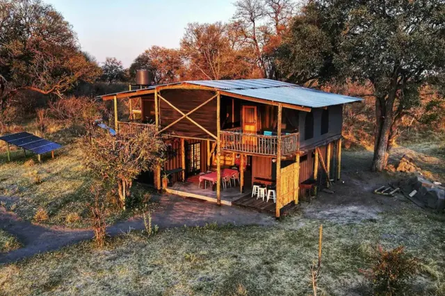 Zweistöckige Holzlodge auf Stelzen in Buschlandschaft bei warmem Seitenlicht