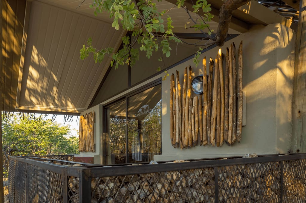Außenbalkon einer Lodge mit Holzverkleidung und Gabionen im warmen Spätnachmittagslicht.
