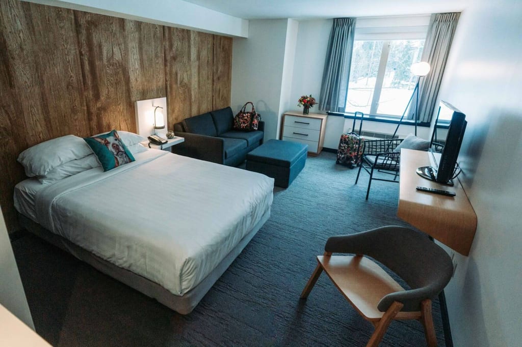 Modernes Hotelzimmer mit Doppelbett, Sofa und Fensterblick bei Tageslicht.