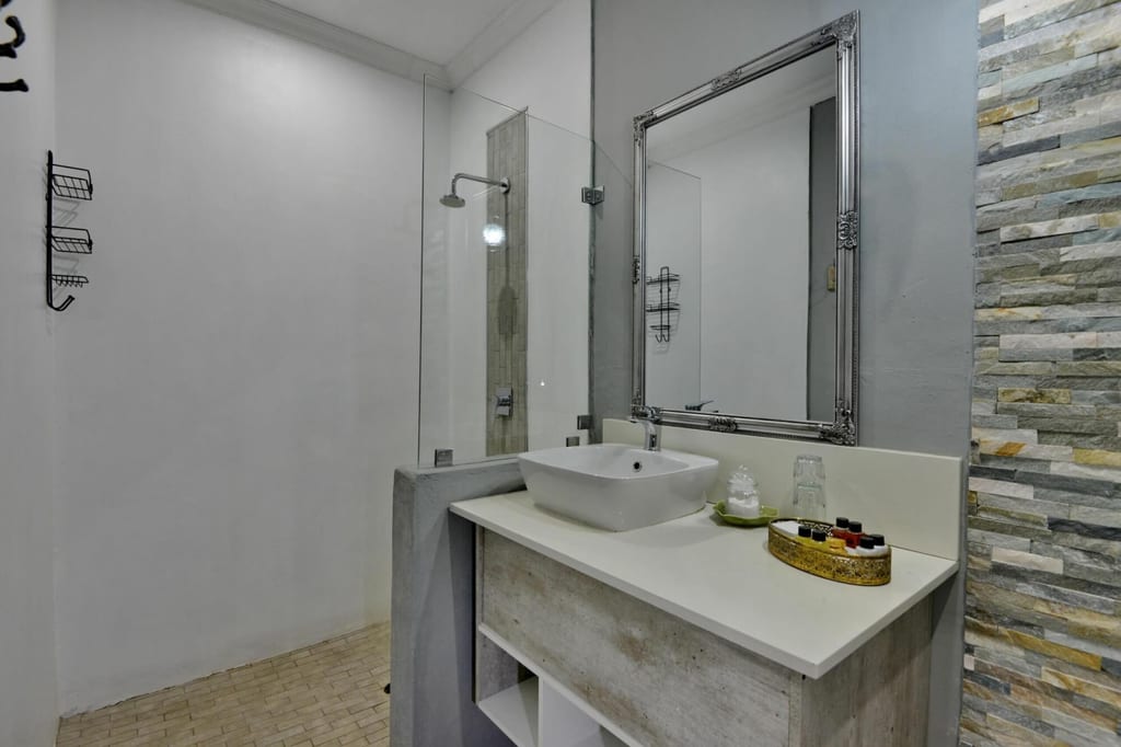 Modernes Badezimmer mit Waschbecken, großem Spiegel und offener Dusche, Natursteinwand rechts.