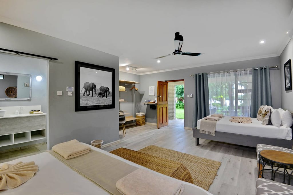Helles Lodgezimmer mit zwei Betten, offener Holztür zum Garten und einem Schwarzweiß-Foto an der Wand.