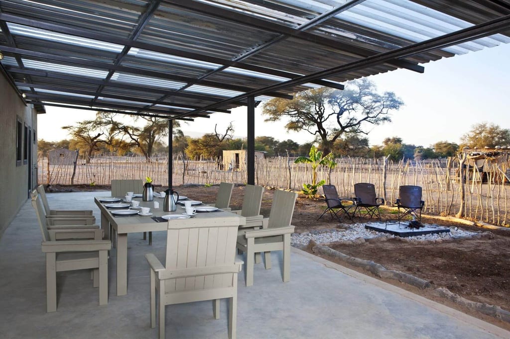 Überdachte Terrasse mit gedecktem Tisch, Stühlen und Feuerstelle vor trockener Landschaft und Bäumen