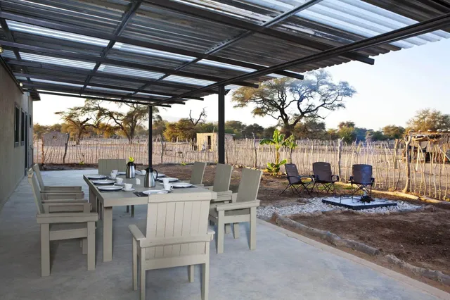 Überdachte Terrasse mit gedecktem Tisch, Stühlen und Feuerstelle vor trockener Landschaft und Bäumen