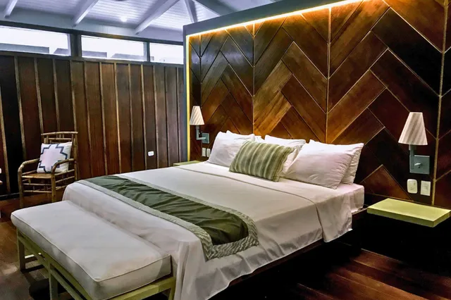 Gemütliches Schlafzimmer mit Doppelbett, grünem Bettläufer und dekorativem Holz-Kopfteil, warmes Licht.