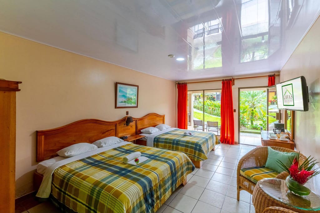 Helles Hotelzimmer mit zwei Betten, roten Vorhängen und Blick auf eine grüne Gartenterrasse.