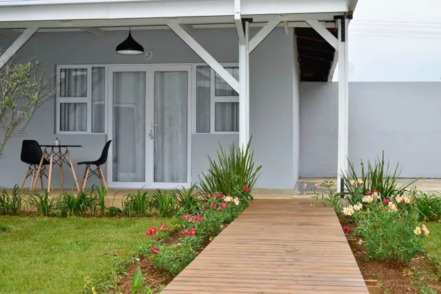Frontalansicht eines Holzstegs zum Eingang mit Veranda, Tisch, Stühlen und blühendem Garten.