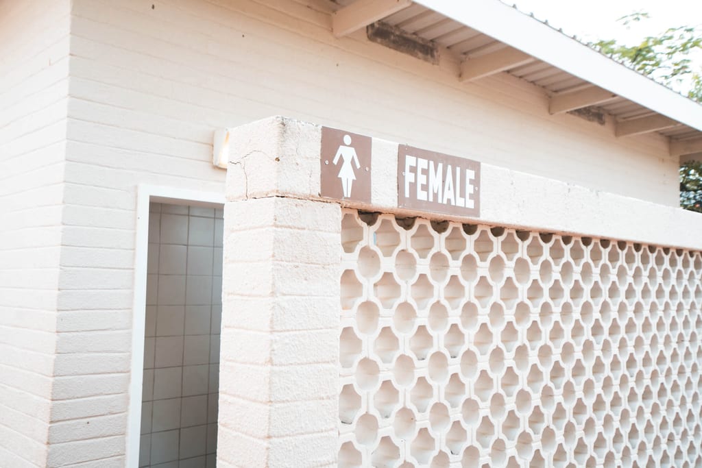 Außenansicht einer öffentlichen Damentoilette mit Schild "FEMALE" und dekorativer weißer Mauer