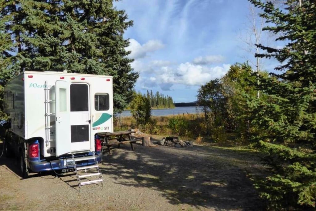 Wohnmobil am Waldrand mit Picknickplatz und Blick auf einen See bei Tageslicht