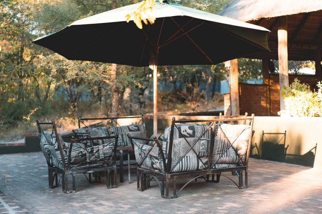 Außenlounge mit gepolsterten Sesseln und großem Sonnenschirm auf gepflasterter Terrasse im warmen Licht.