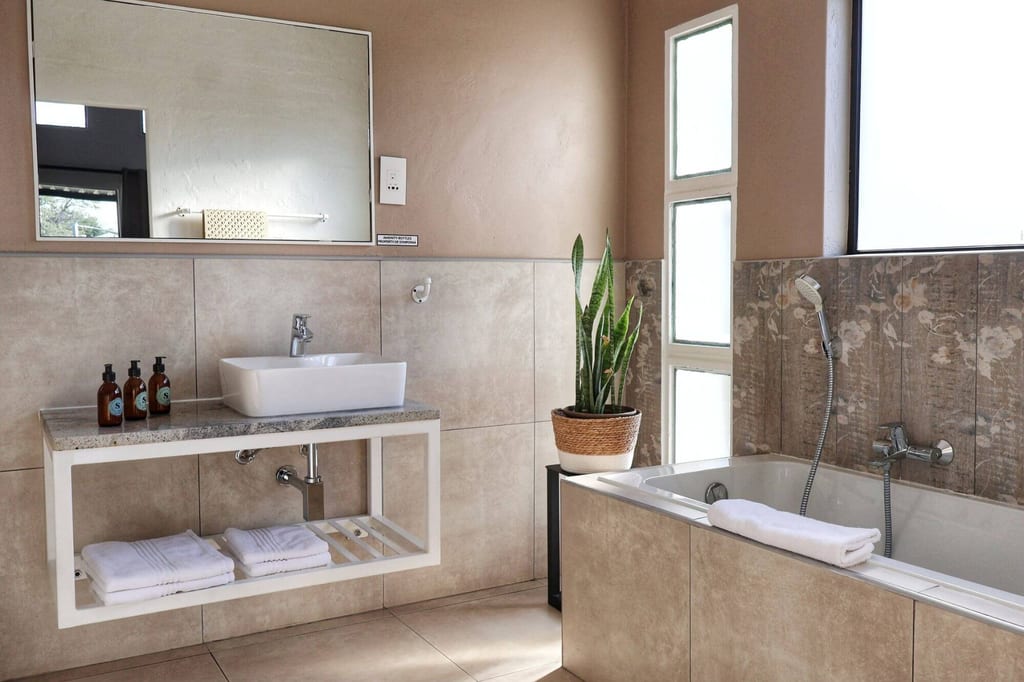 Modernes, helles Badezimmer mit Waschbecken, Badewanne und Zimmerpflanze, Tageslicht von rechts.