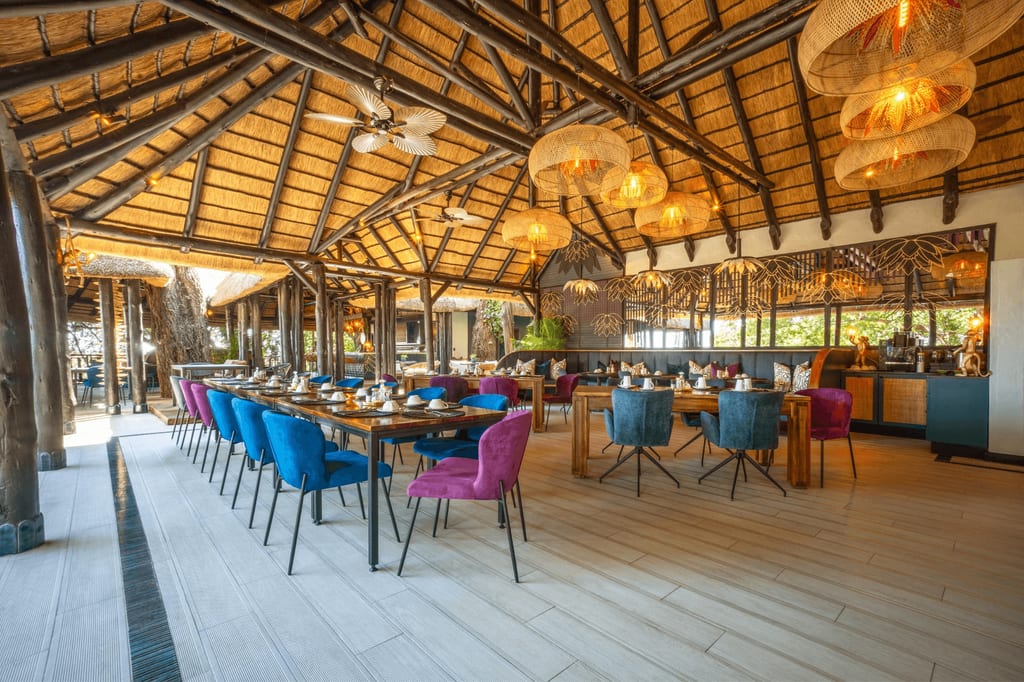 Offenes Restaurant mit Strohdach, bunten Polsterstühlen und warmen Hängeleuchten