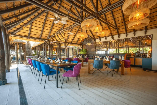 Offenes Restaurant mit Strohdach, bunten Polsterstühlen und warmen Hängeleuchten