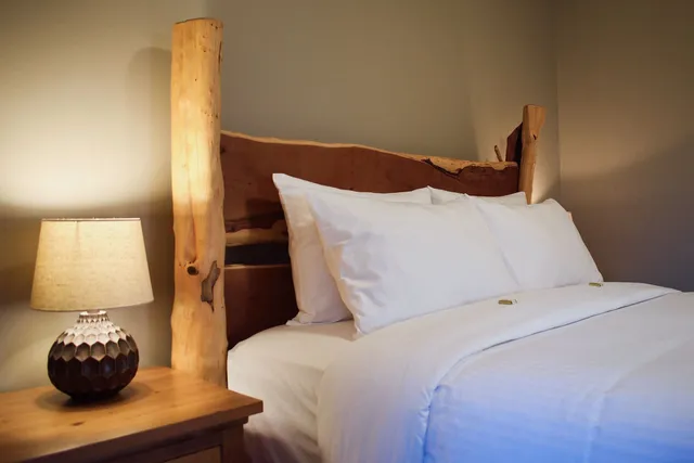 Gemütliches Schlafzimmer mit naturbelassenem Holzkopfteil, weißer Bettwäsche und warm beleuchteter Nachttischlampe.