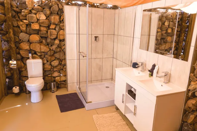 Modernes Badezimmer mit Duschkabine, Doppelwaschtisch und Natursteinwänden in warmem Licht.