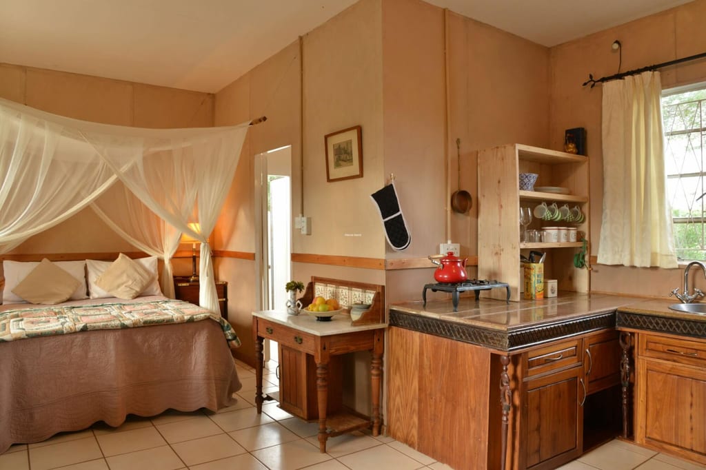 Kombinierter Schlaf- und Küchenraum mit Moskitonetz über dem Bett und Holzküche bei Tageslicht