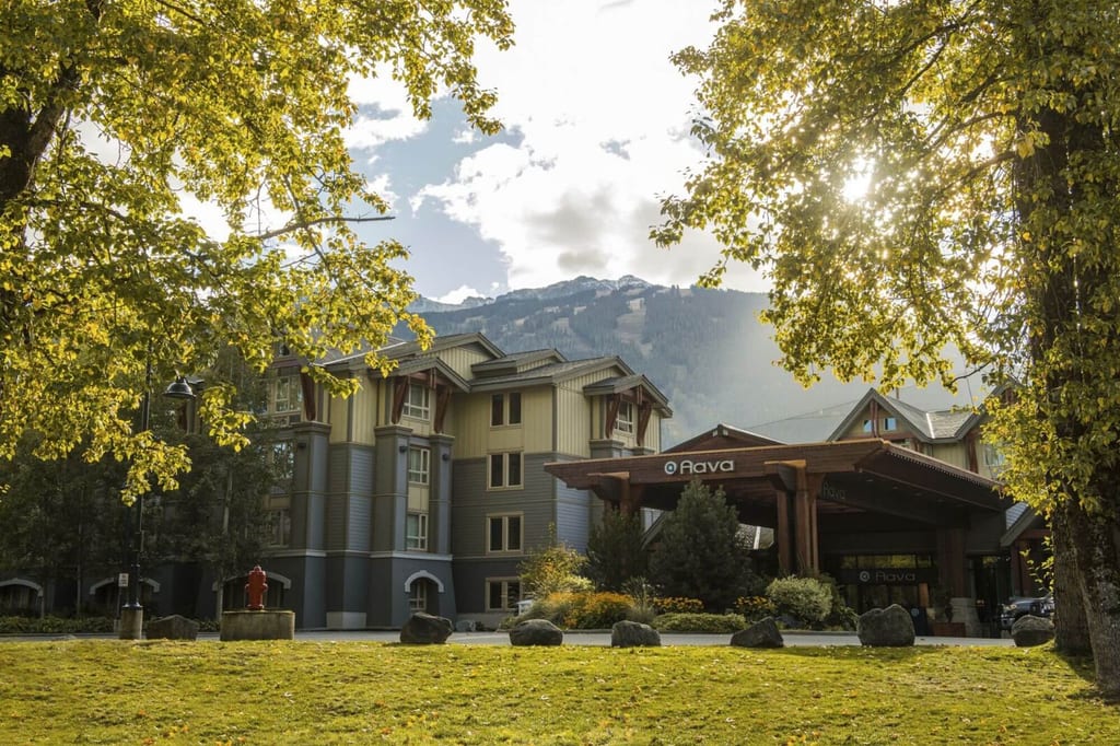 Hotel mit überdachtem Eingang, Rasen im Vordergrund und Bäume im warmen Spätnachmittagslicht.
