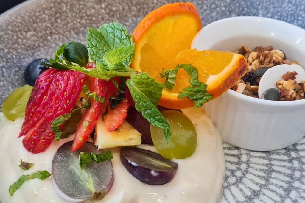 Nahaufnahme von Joghurt mit Früchten, Minze und Granola auf einem Teller
