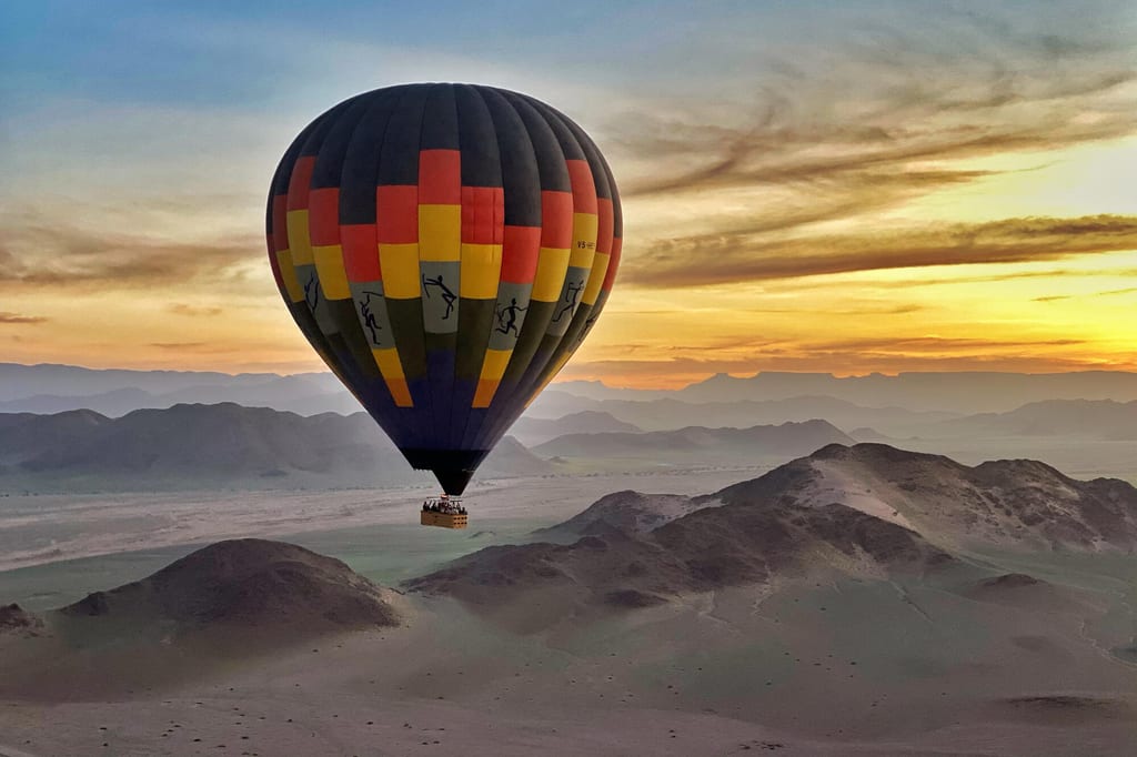 Bunter Heißluftballon über sandiger Wüstenlandschaft im warmen Licht bei Sonnenaufgang