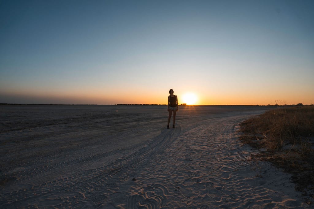Einzelne Person als Silhouette auf weiter Sandfläche bei tief stehender Sonne, lange Schatten und ruhige Stimmung.