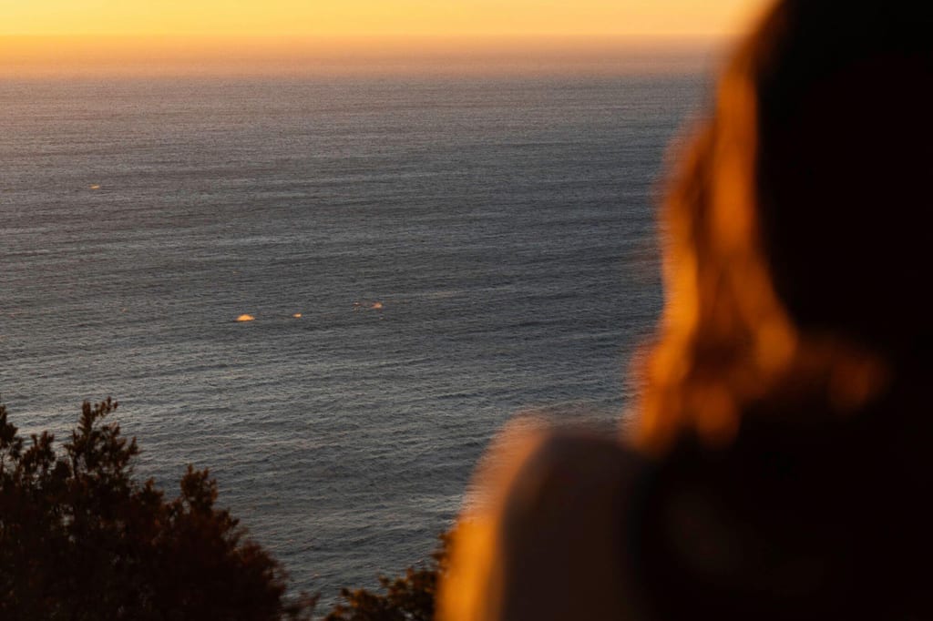 Unscharfe Person blickt bei Sonnenuntergang aufs ruhige Meer mit goldenem Horizont
