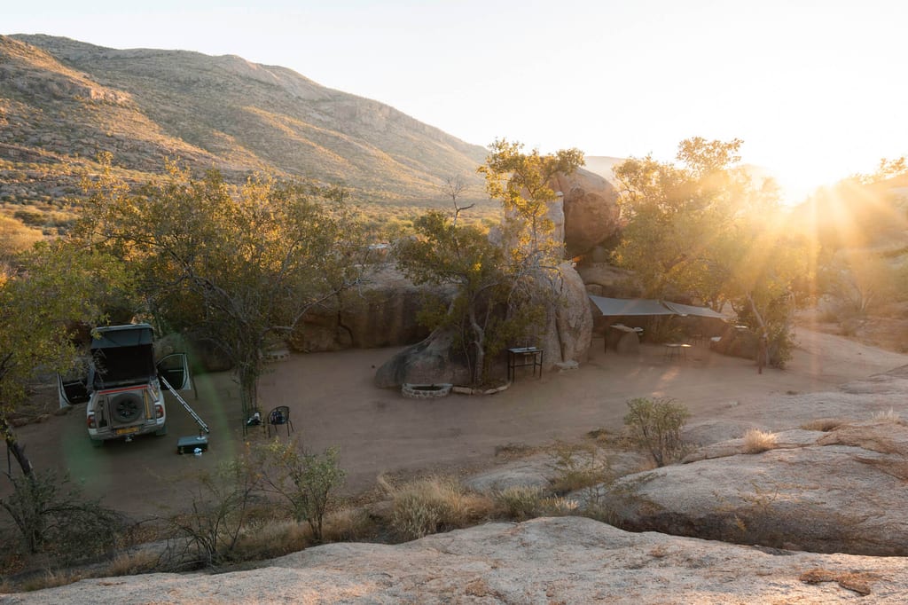 Campinglager mit Geländewagen zwischen Granitfelsen im goldenen Licht des Erongo-Gebirges, Namibia.