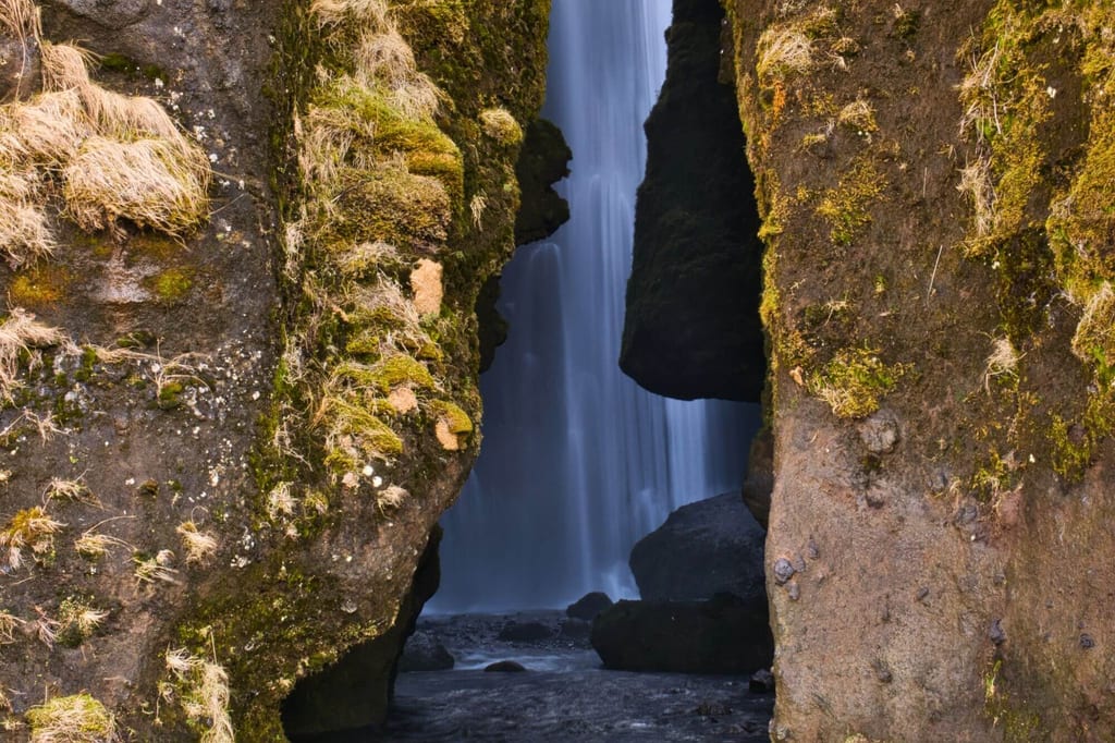 Wasserfall sichtbar durch enge, moosbewachsene Felsspalte, ruhige Langzeitbelichtung