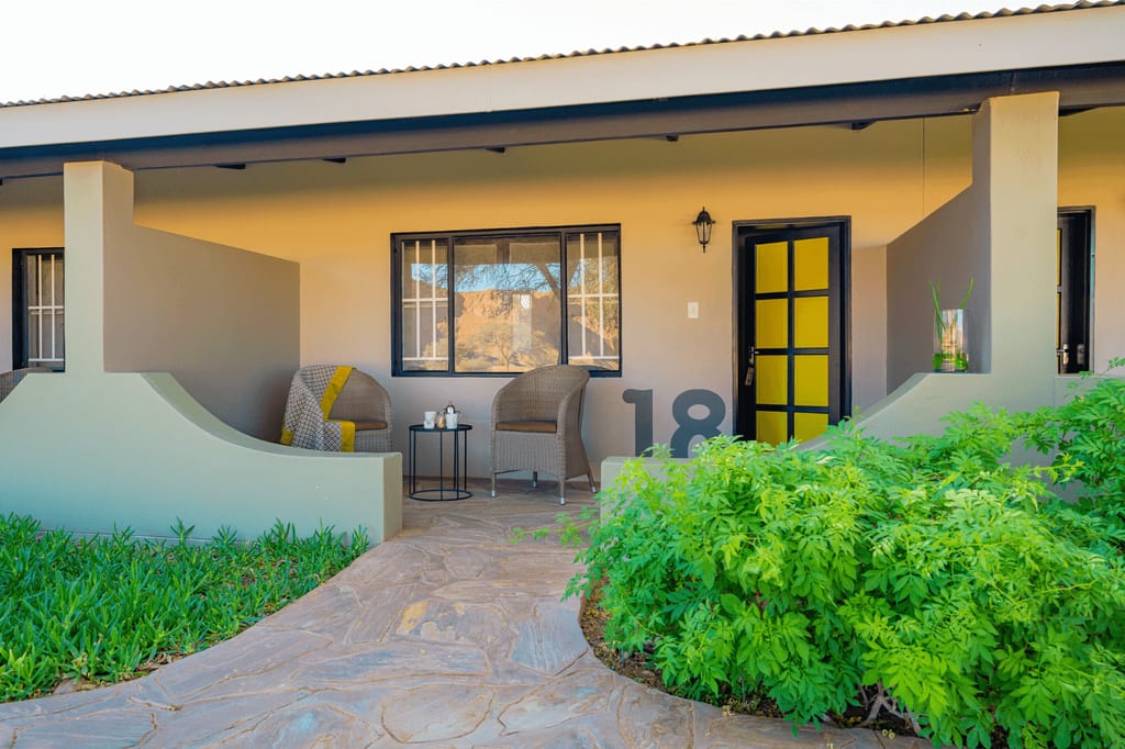 Vorgarten und Terrasse eines Bungalows mit zwei Korbsesseln, gelber Tür und Hausnummer 18