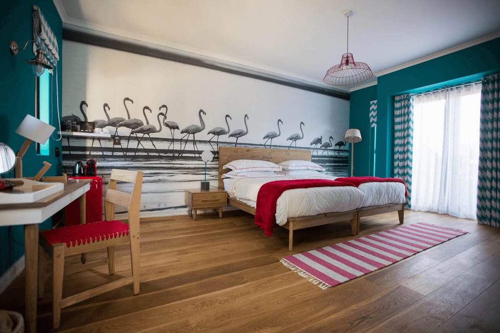 Helles Schlafzimmer mit Doppelbett, türkisfarbenen Wänden und großem Wandbild mit Vögeln.