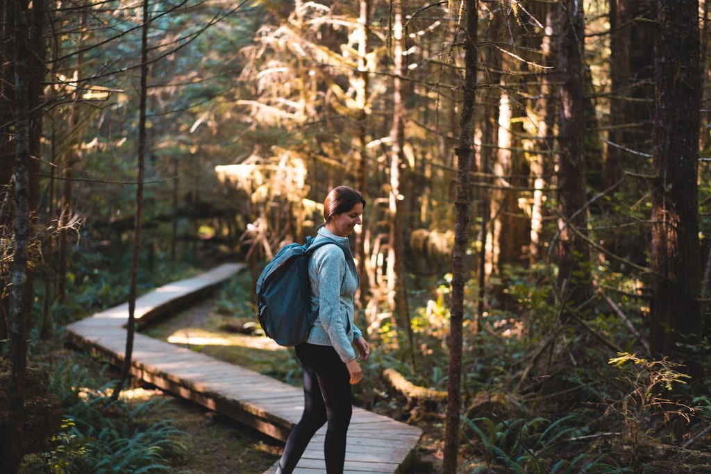 Wanderin mit Rucksack auf hölzernem Bohlenweg im moosigen Wald bei warmem Seitlicht.