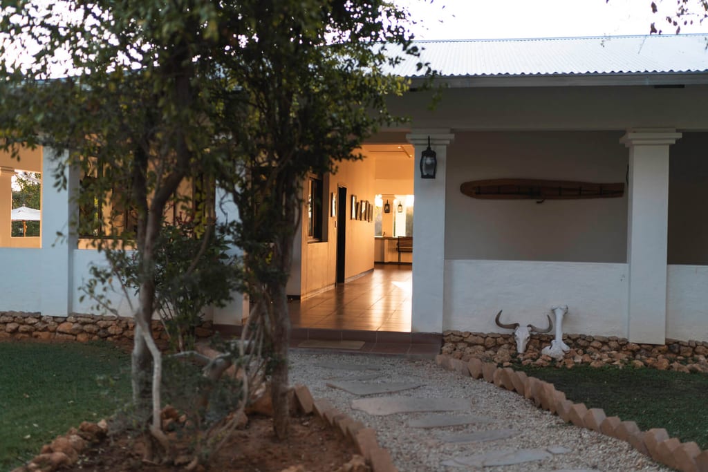 Eingangsbereich eines Hauses bei Dämmerung mit Kiesweg, warmer Innenbeleuchtung und Tierschädeln an der Wand.