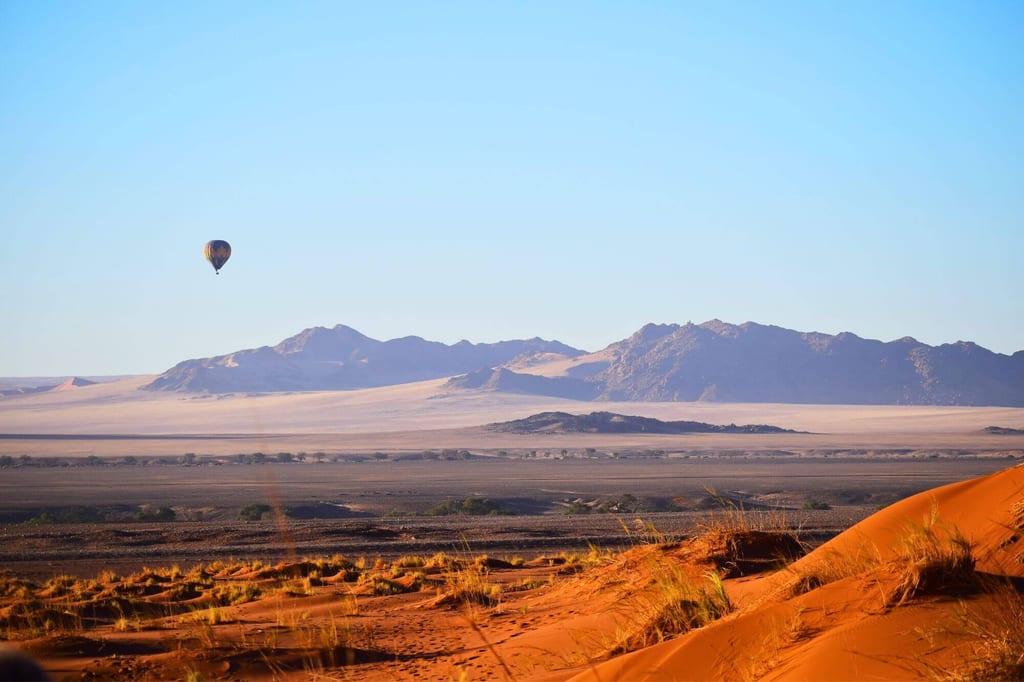 Ein Heißluftballon gleitet über die rote Dünenlandschaft
