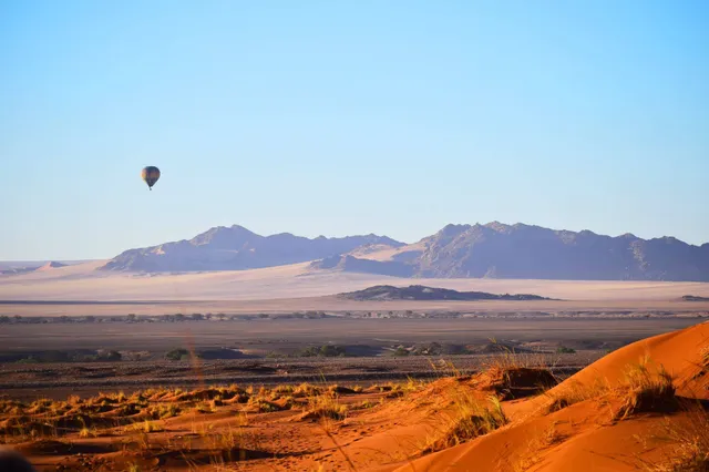 Ein Heißluftballon gleitet über die rote Dünenlandschaft