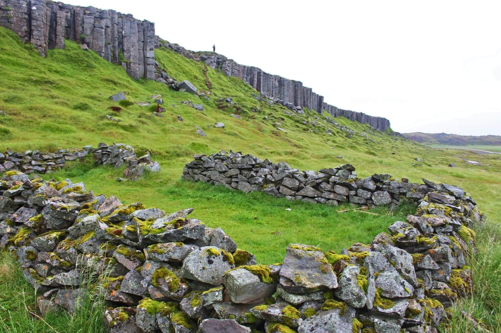 Moosbewachsene Trockensteinmauer vor senkrechten Basaltklippen unter bedecktem Himmel