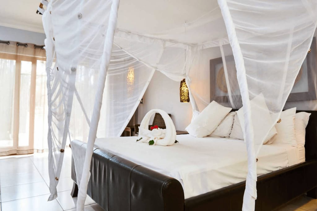 Helles Hotelzimmer mit Doppelbett unter weißem Moskitonetz und Handtuch-Schwan auf der Decke.