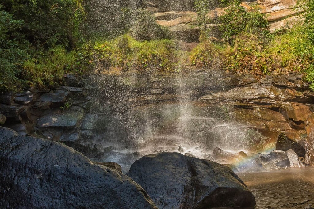 Nahaufnahme eines Wasserfalls über Felsen mit Sprühnebel und schwachem Regenbogen