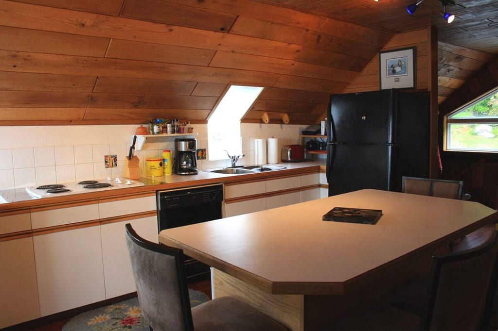 Gemütliche Dachgeschossküche mit Kücheninsel, Holzdecke und Kühlschrank, beleuchtet von Dachfenstern.