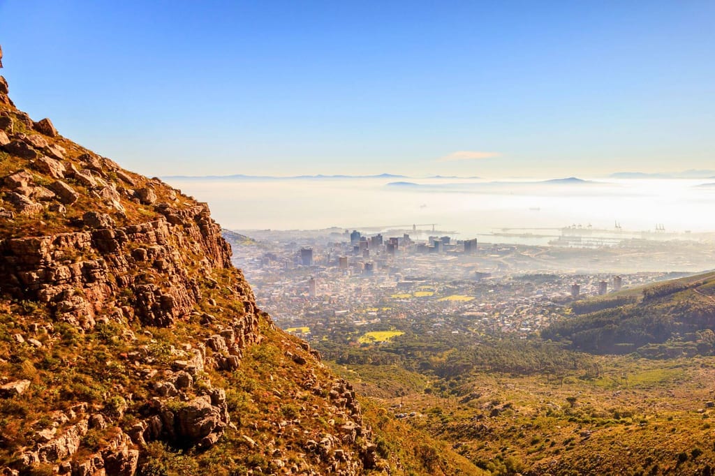 Panoramablick von felsigem Berghang auf nebelverhangene Stadt und Meer im warmen Licht