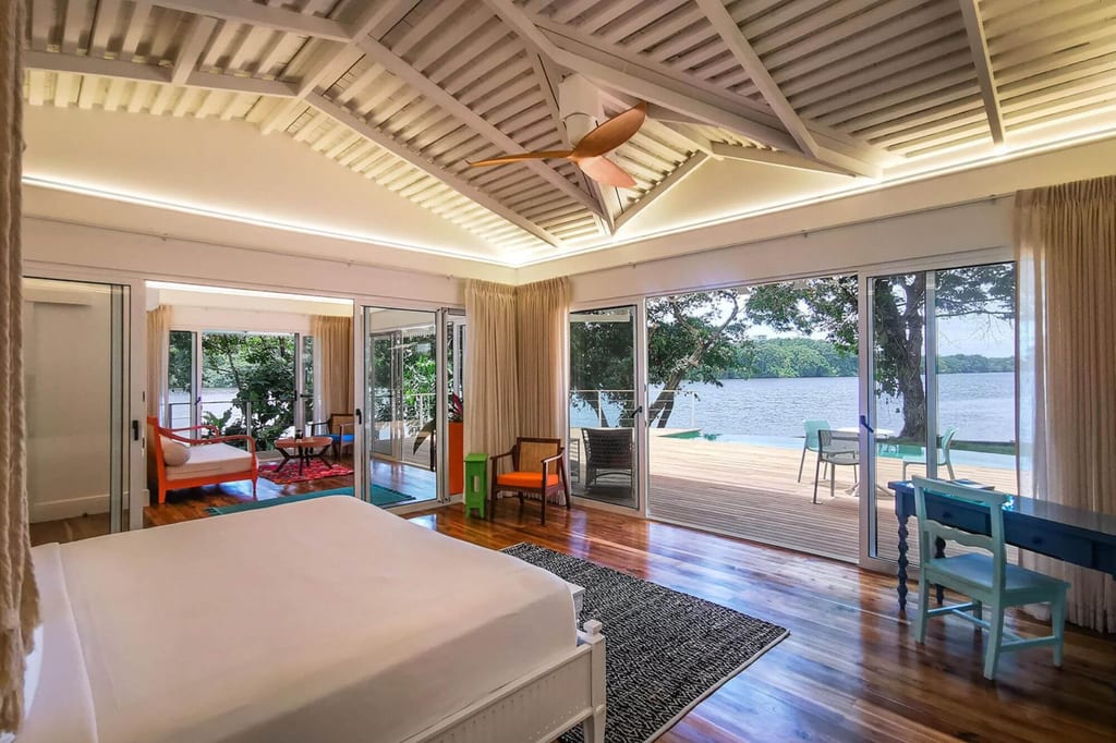 Helles Schlafzimmer mit großen Glasschiebetüren und Blick auf Terrasse und See.
