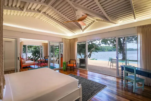 Helles Schlafzimmer mit großen Glasschiebetüren und Blick auf Terrasse und See.